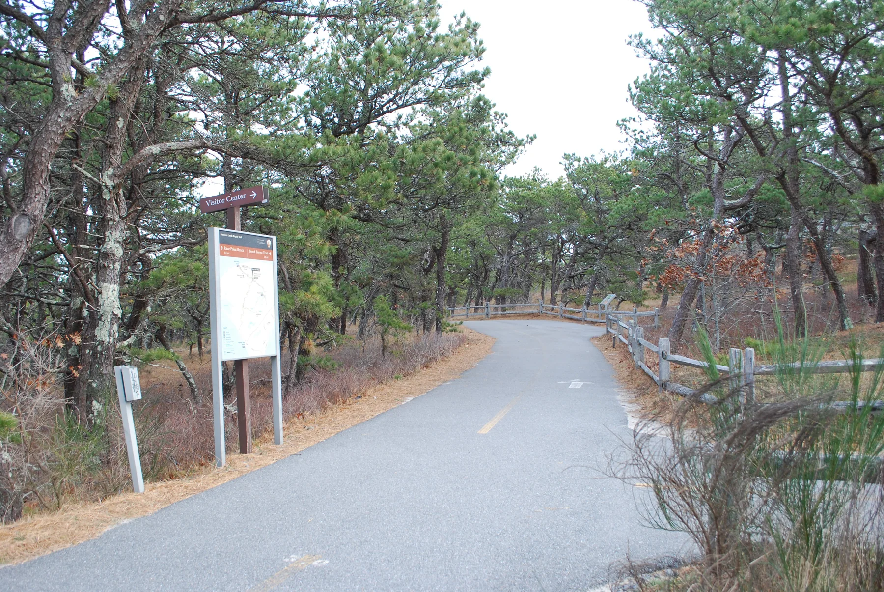 Entrance to the paved bike trail with regulation signage and trees.