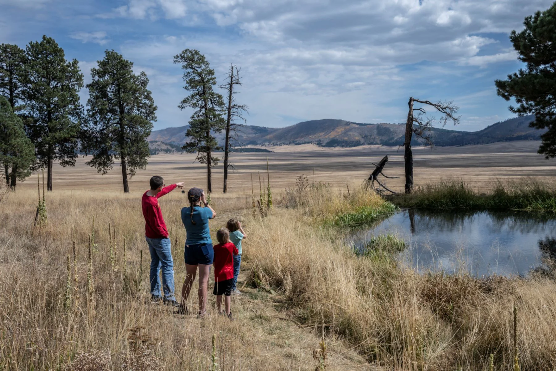 A family with young children stands beside a pond overlooking a vast grassland.