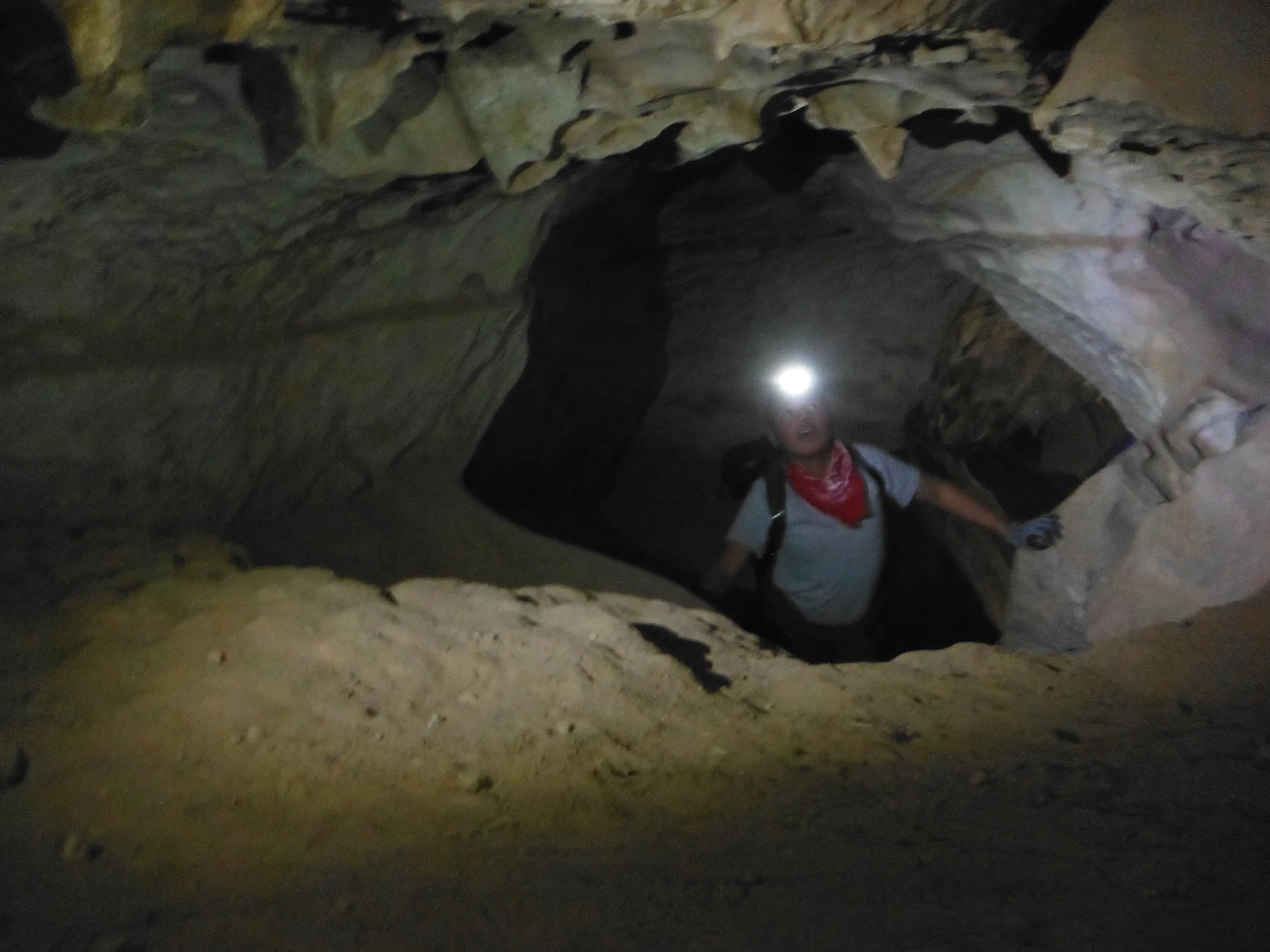 Male student with headlamp looking at cave formations on the ceiling.